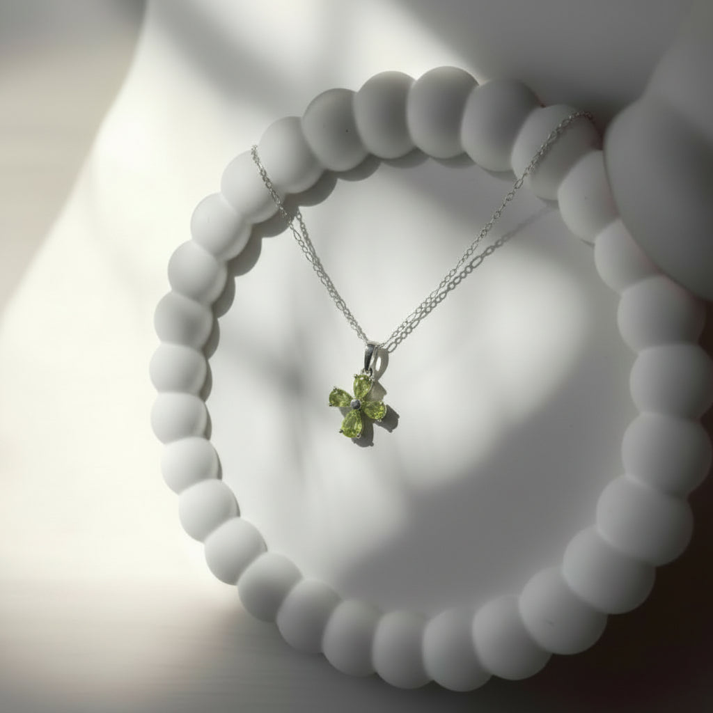 Necklace with a green pendant on a white beaded bracelet against a neutral background