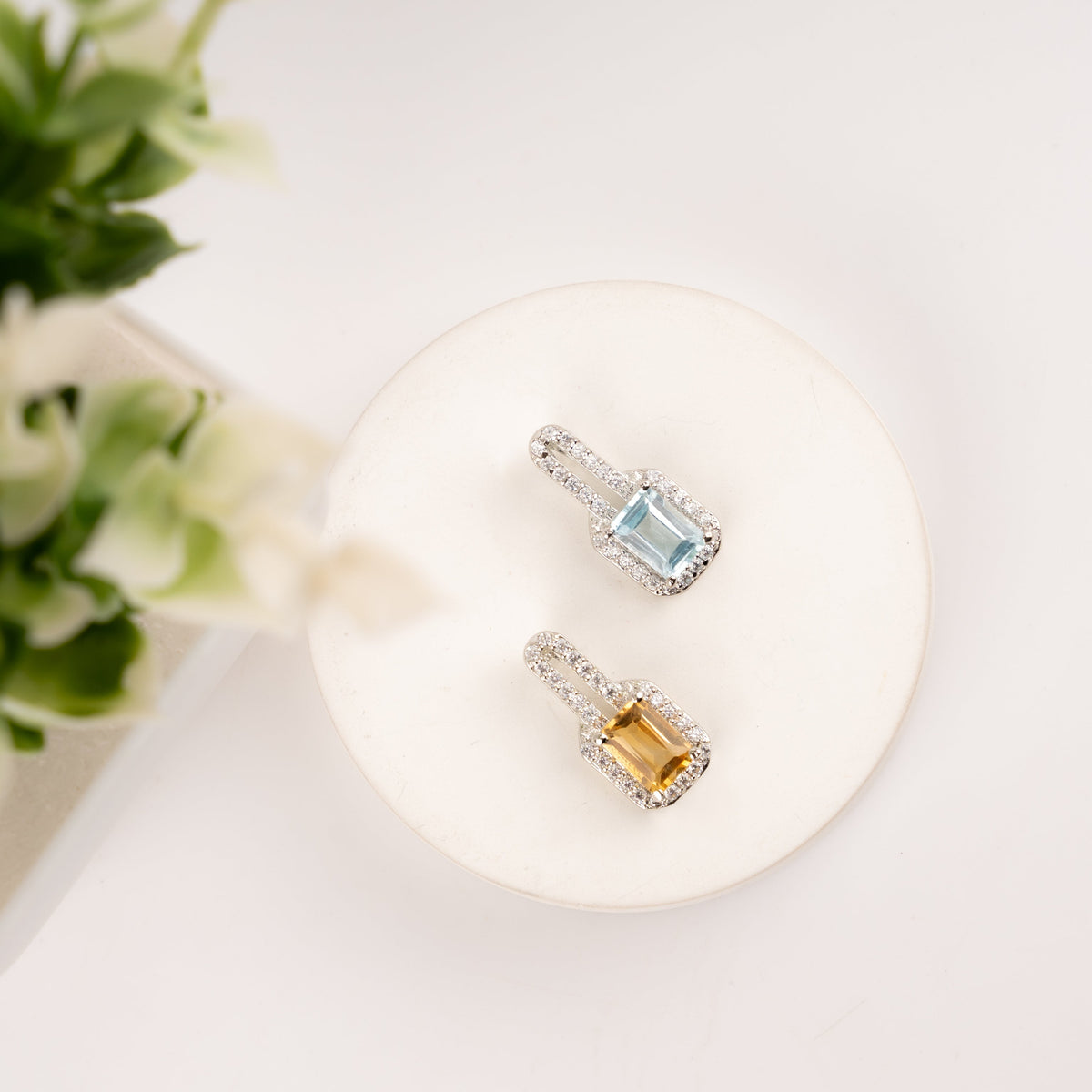 Top view of two emerald-cut halo pendants - sky blue topaz and golden citrine with diamond halo on white display