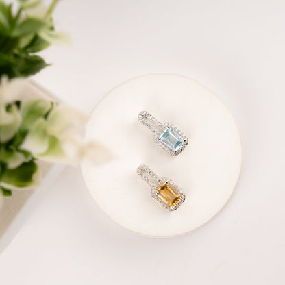 Top view of two emerald-cut halo pendants - sky blue topaz and golden citrine with diamond halo on white display