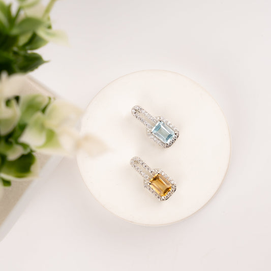 Top view of two emerald-cut halo pendants - sky blue topaz and golden citrine with diamond halo on white display