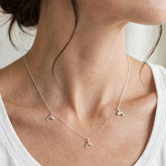 A close-up of a woman wearing a delicate silver necklace with three small crescent moon charms, styled with a white tank top.