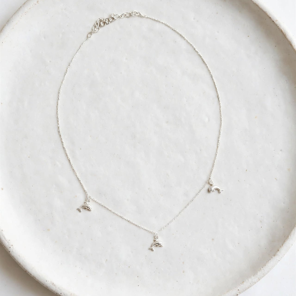 A delicate silver necklace with three small butterfly charms, displayed on a textured white ceramic plate against a clean white background.
