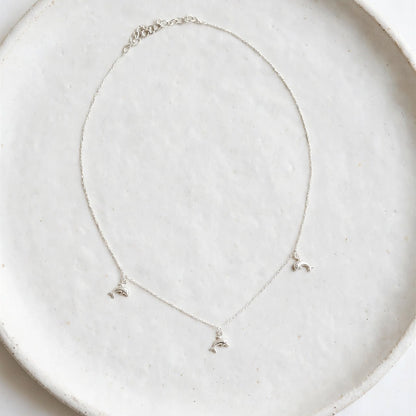 A delicate silver necklace with three small butterfly charms, displayed on a textured white ceramic plate against a clean white background.