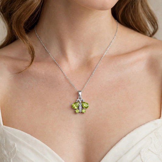 A close-up of a woman wearing a delicate silver chain necklace with a green floral pendant, paired with a white lace-trimmed top.