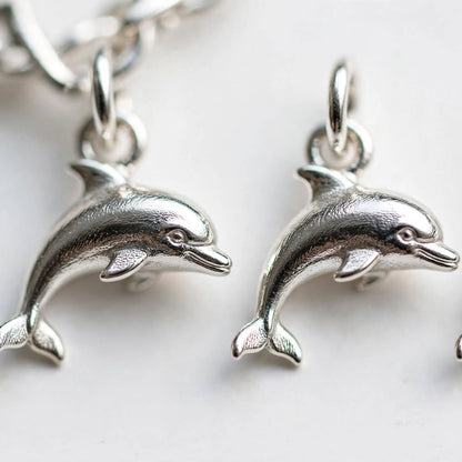 Three silver dolphin charms with attached jump rings, shown on a white background with part of a silver chain visible at the top left.