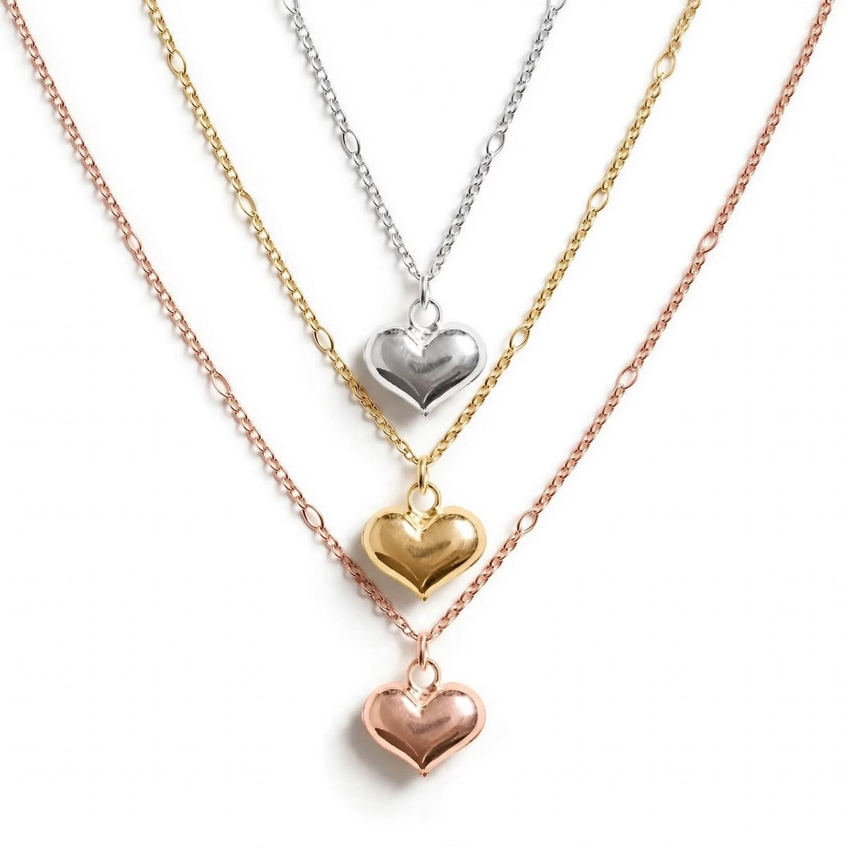 Three heart-shaped pendant necklaces on delicate chains, shown in rose gold, yellow gold, and silver metal finishes against a clean white background.